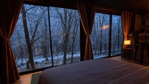 A bedroom with a large window, a bed, curtains, a nightstand, and a lamp. - L'Ange De Fer (immersion totale en pleine forêt) (Illoud)