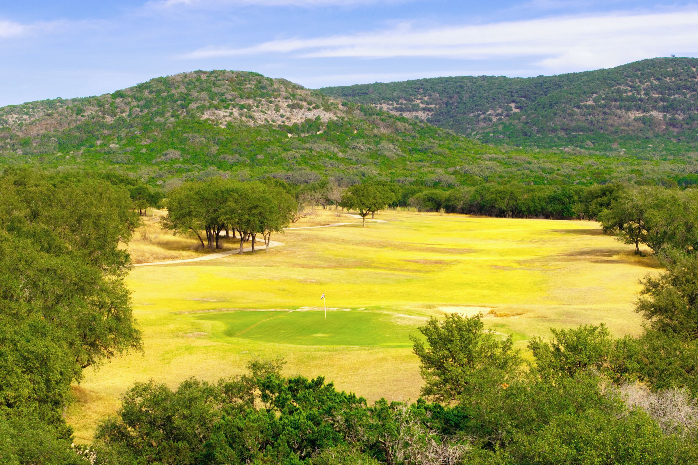 Un parcours de golf entouré d’une végétation luxuriante et de collines verdoyantes en arrière-plan.