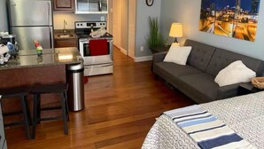 Un espacio habitable pequeño con kitchenette, un sofá y un cuadro con vista urbana.