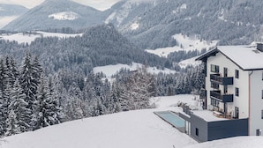 A modern two-story building with a balcony, surrounded by snow-covered mountains and trees. - Penthouse With Shared Pool (Sankt Martin am Tennengebirge)