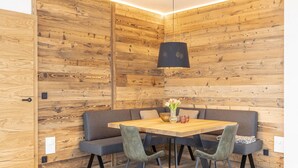 A modern dining area with a wooden wall, a round table, four chairs, and a hanging light fixture. - Penthouse With Shared Pool (Sankt Martin am Tennengebirge)