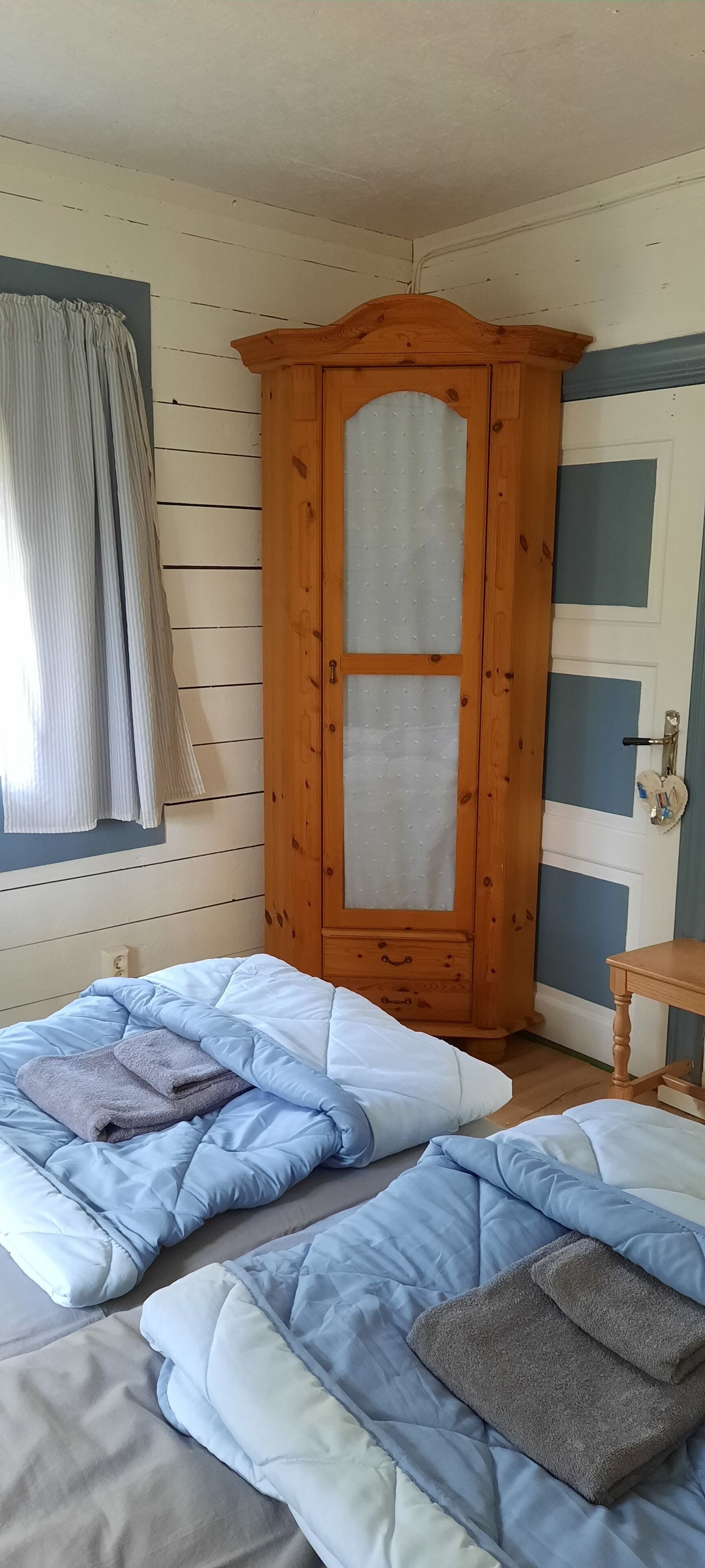 Ein Schlafzimmer mit zwei Betten, einem Holzschrank, einem kleinen Tisch und einem Fenster mit Vorhängen.