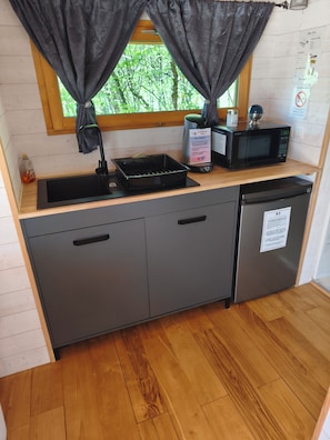 A compact kitchen with a sink, a microwave, a small refrigerator, and a window with curtains.