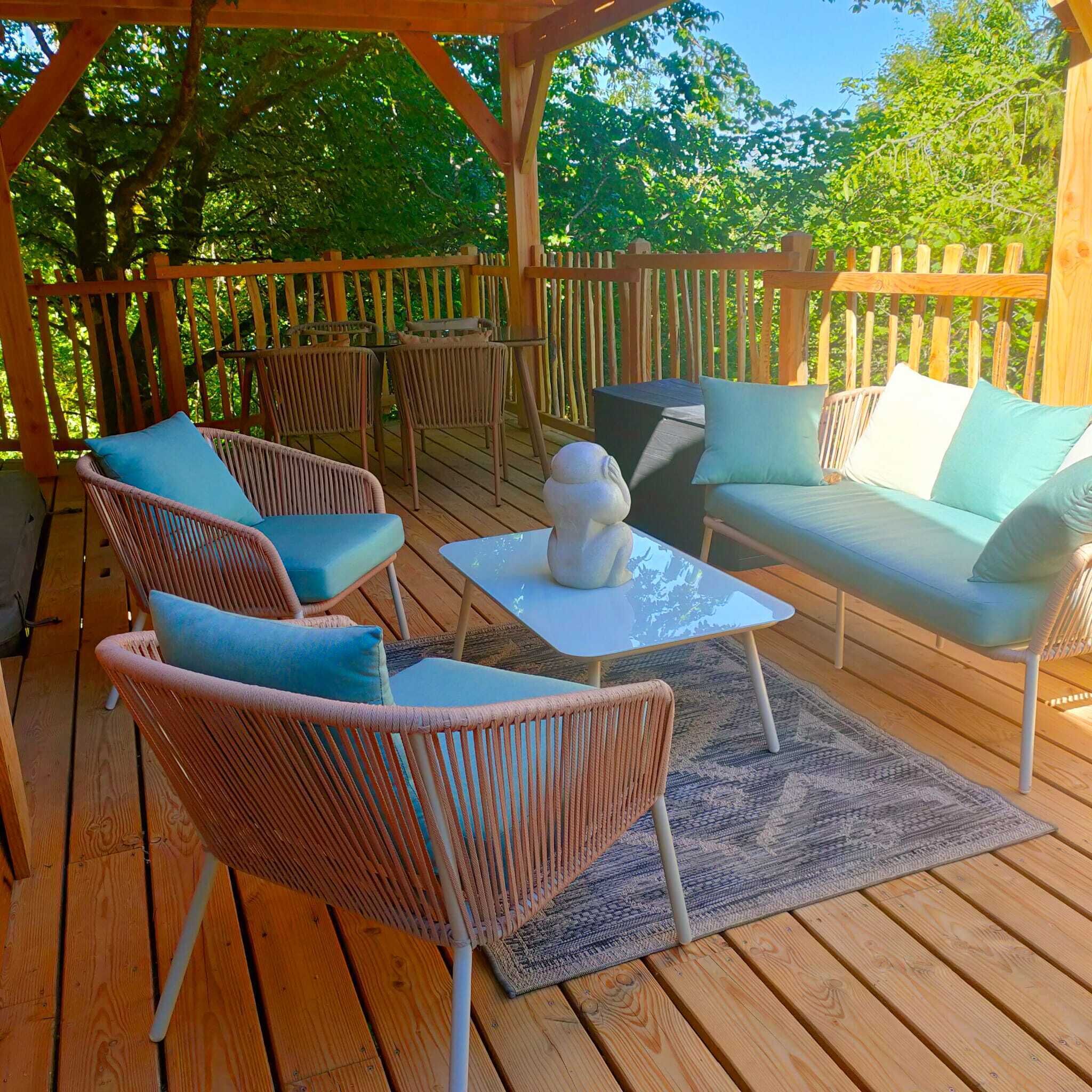 Une terrasse en bois avec des meubles en osier, notamment des chaises et un canapé, ainsi qu’une petite table.
