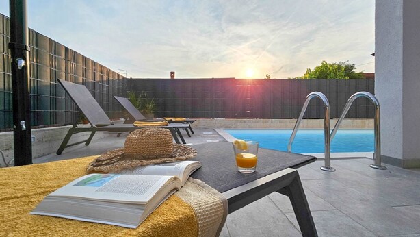 A rooftop pool area with lounge chairs, a table with a book and drink, and a view of the sunset. - Exquisite villa with private pool, BBQ, table football and en suite bathrooms (Fiorini)