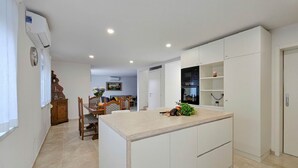 A modern kitchen with white cabinetry, a central island, and a dining area with a wooden table and chairs. - Exquisite villa with private pool, BBQ, table football and en suite bathrooms (Fiorini)