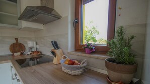 Een keuken met een raam, een bloempot, een mand met fruit en een messenblok.