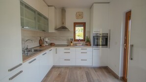 Een moderne keuken met witte kasten, een roestvrijstalen spoelbak, een ingebouwde oven en een raam met uitzicht op groen.