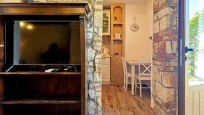 Une pièce chaleureuse avec un mur en pierre, un meuble TV en bois, un coin repas avec une table et des chaises, et une horloge au mur.