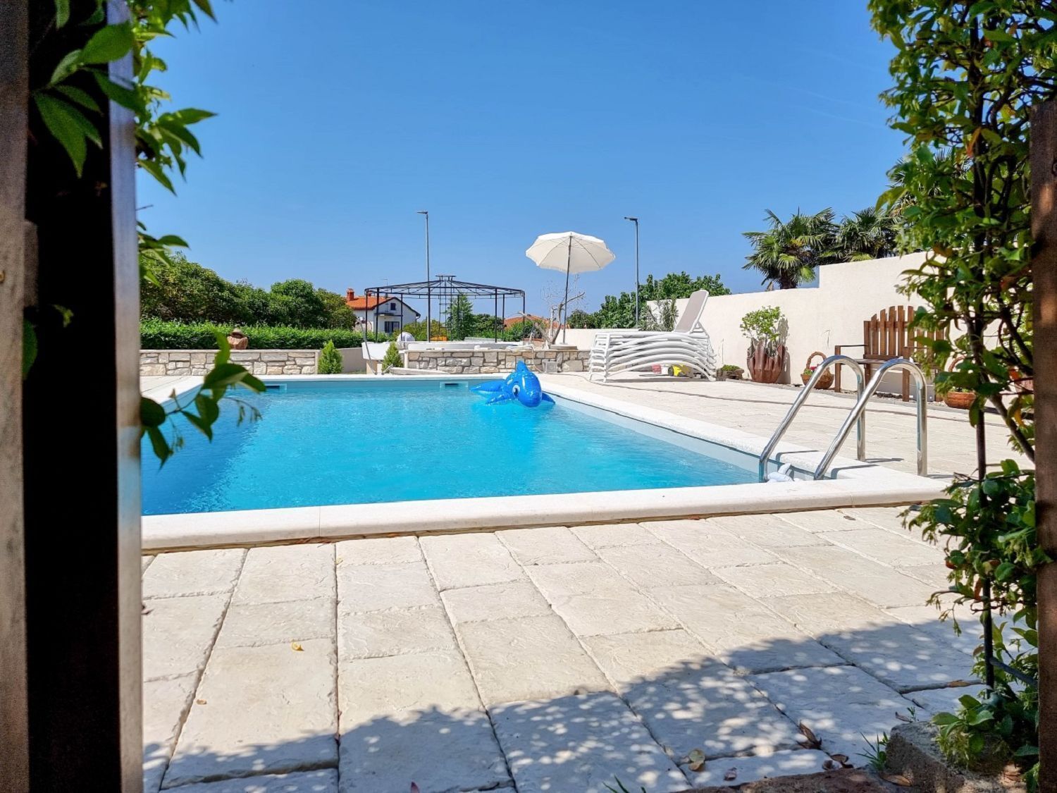 Une piscine avec un jouet gonflable bleu, un parasol blanc et une échelle en métal.