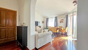 Een woonkamer met een bank, een eettafel met stoelen, een houten garderobe en een televisie.