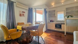 Een moderne keuken met een ingebouwde oven en een eethoek met een houten tafel en gele stoelen.