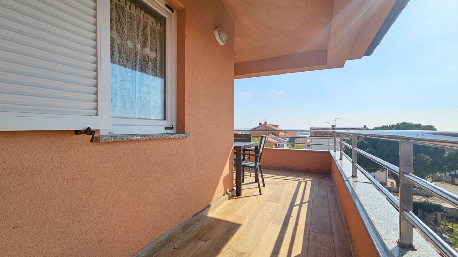 Un balcon doté d’un plancher en bois, d’une rambarde en métal et offrant une vue sur les bâtiments environnants.