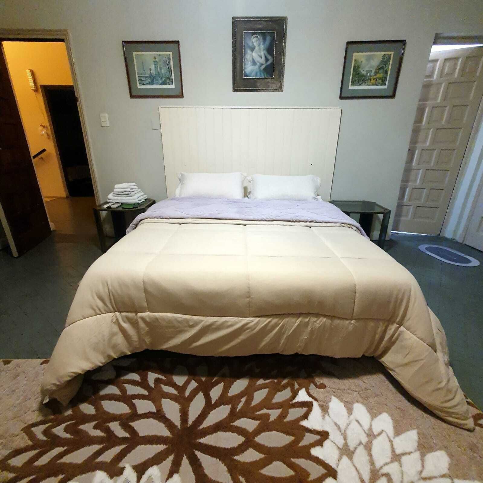 A hotel room with a large bed, a bedside table, a nightstand, and a door.