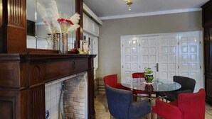 Uma sala de jantar com uma mesa redonda de vidro, cadeiras vermelhas e azuis, uma lareira e um candelabro.