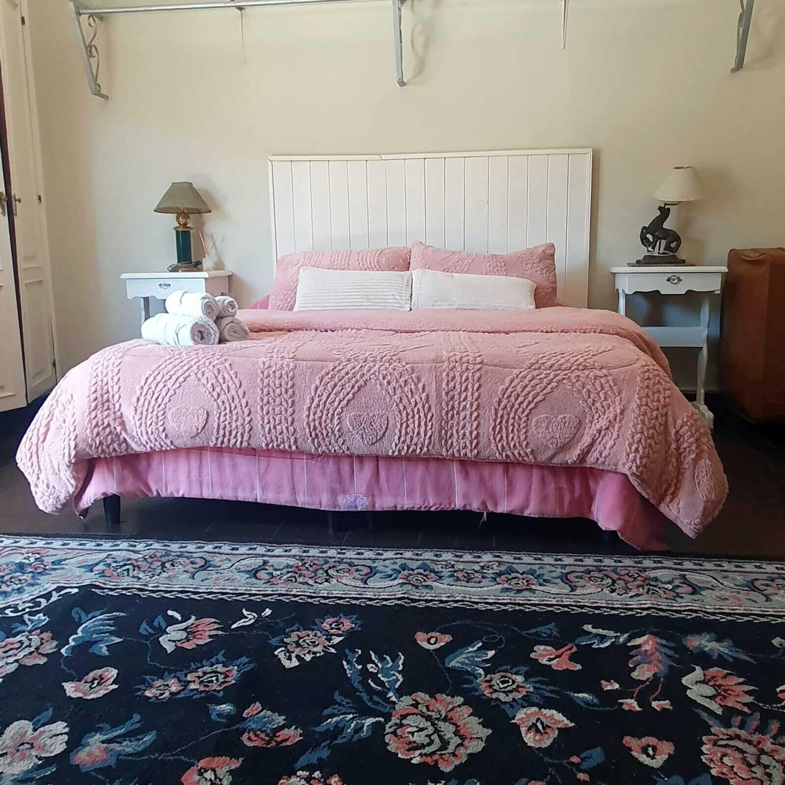 Ein Bett mit einer rosa Steppdecke, einem weißen Kopfteil und einem Teppich mit Blumenmuster.