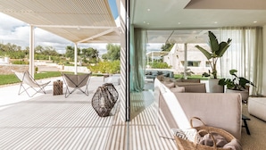 Ein moderner Außenbereich mit einer Pergola, einer Sitzecke und Blick auf ein Steinhaus.