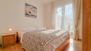 Quarto com cama, mesa de cabeceira, abajur e janela com cortinas.