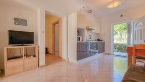 Uma sala de estar moderna com televisão de tela plana, um armário de madeira e um espaço de jantar com mesa e cadeiras vermelhas.