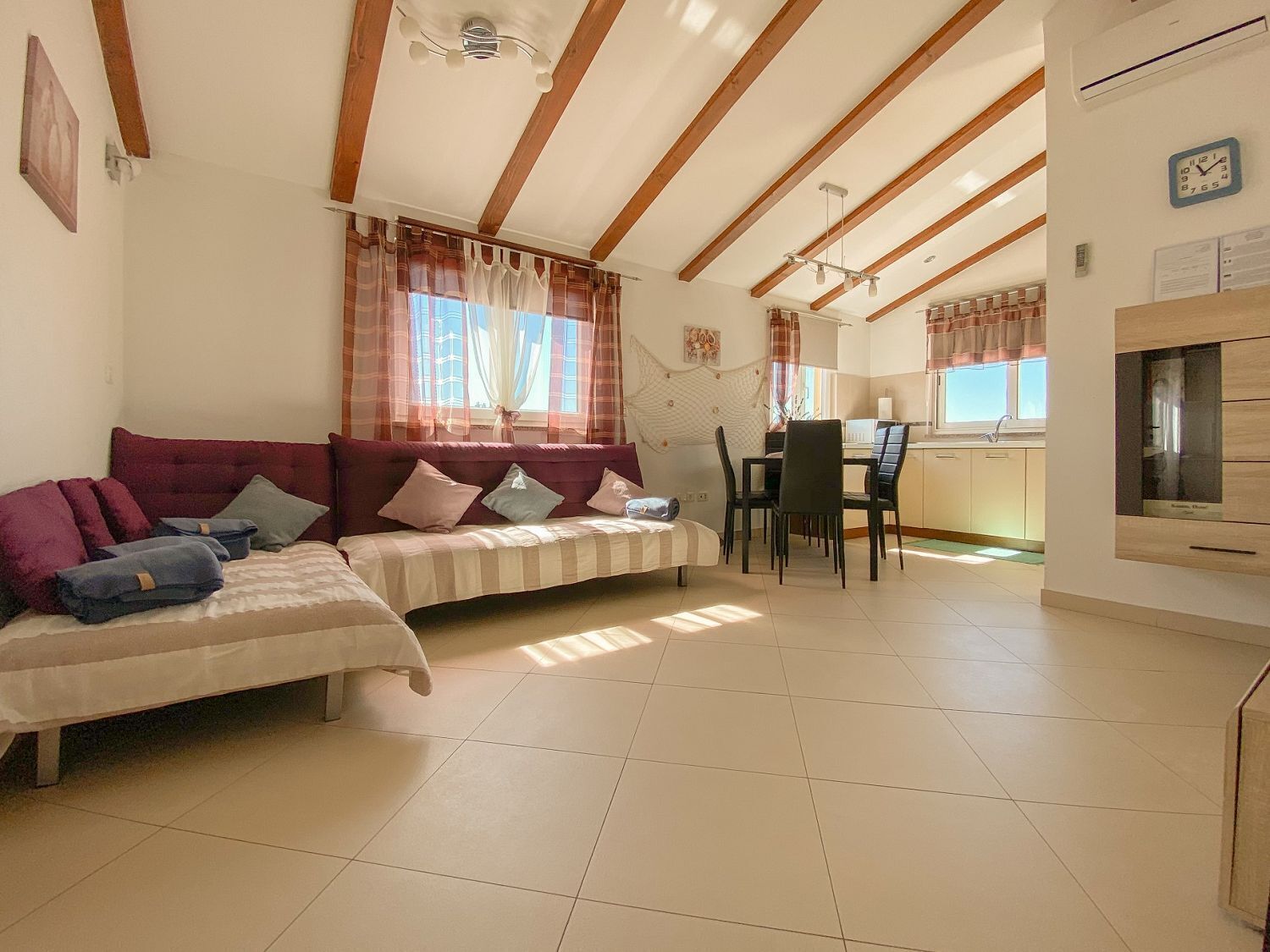 A cozy living room with a sofa, a dining area with a table and chairs, and a kitchen area with cabinets and a window.