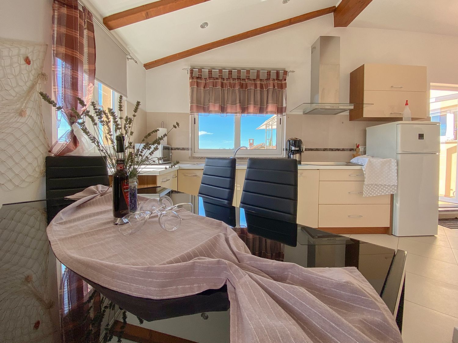 A modern kitchen with a dining area, featuring a glass table, chairs, and a view of the outside.