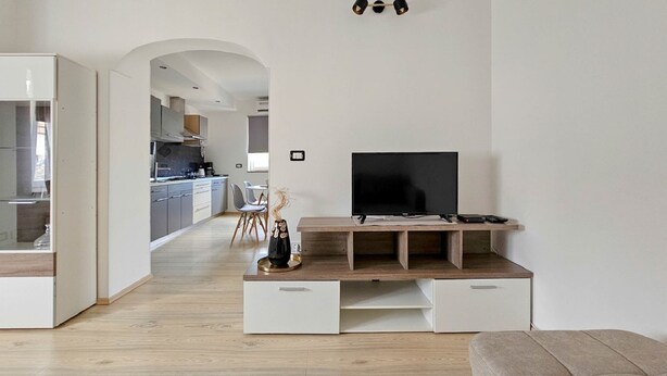 A modern living room with a TV on a wooden stand, a white sofa, and a kitchen in the background. - Apartment Vili (Novigrad)