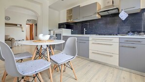 A modern kitchen with grey cabinets, a white countertop, and a round dining table with two chairs. - Apartment Vili (Novigrad)