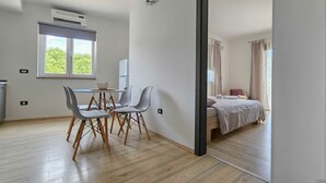 A modern room with a dining area, a bed with a view, and a window with curtains. - Apartment Vili (Novigrad)