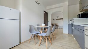 A compact kitchen with a white refrigerator, grey cabinets, and a small dining area with two grey chairs and a white table. - Apartment Vili (Novigrad)