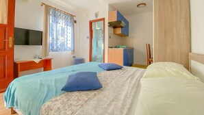 Une chambre à coucher comprenant un lit, un bureau, une télévision, une fenêtre avec des rideaux et un coin cuisine.
