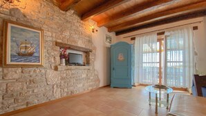 A room with a stone wall, a television on a shelf, a blue door, and a glass table. - Breathtaking sea views and only 30 metres to the beach (Novigrad)