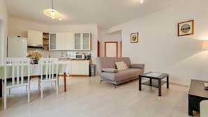 Una sala de estar moderna con un sofá, una mesa de comedor con sillas, una zona de cocina con armarios y una mesita con una lámpara.