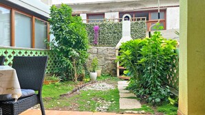 Un pequeño jardín al aire libre con una silla de mimbre, un muro de piedra y diversas plantas.