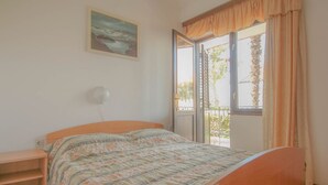 Un dormitorio con cama, ventana con cortinas, un cuadro en la pared y un balcón.