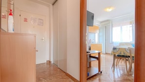 A hotel room with a wooden wardrobe, a small table, a chair, a bed, and a window with a view of the outside.