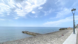 A coastal promenade with a clear sky, a stone walkway, and a lamp post.