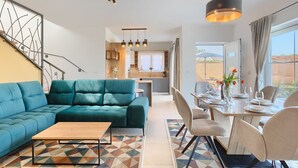 Una sala de estar moderna con un sofá color turquesa, una mesa de centro de madera y un comedor con mesa dispuesta para cuatro.