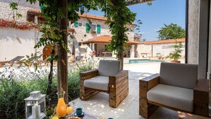 Une terrasse avec deux canapés, une table où sont disposées des boissons et des pâtisseries, et une piscine en arrière-plan.