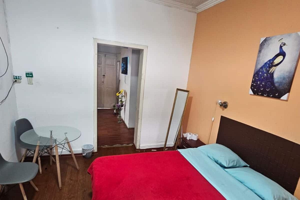 A hotel room with a bed, a TV, a desk with chairs, and a door leading to a hallway.