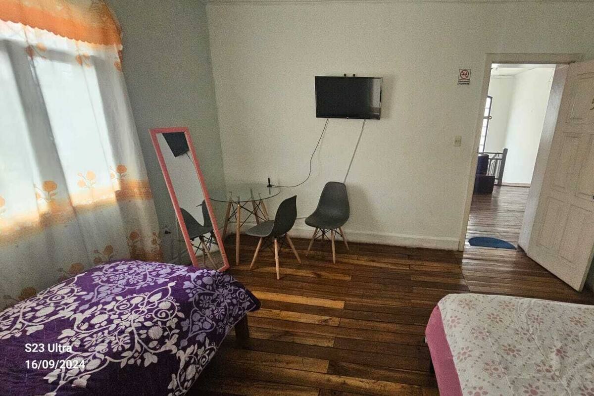 A room with a bed, a desk, two chairs, a television, and a door.