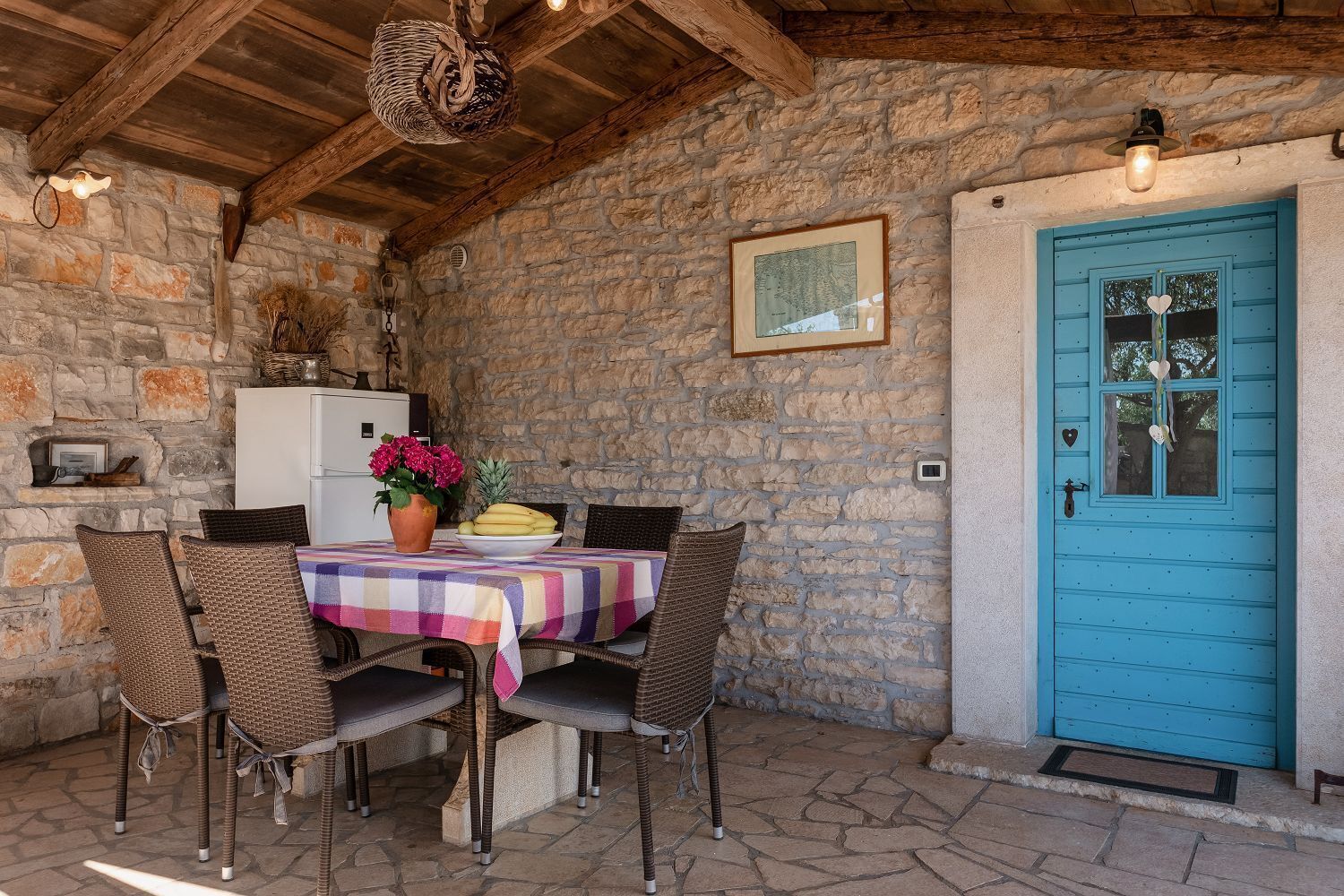 A rustic stone-walled room with a table set for two, a blue door, and a white refrigerator.