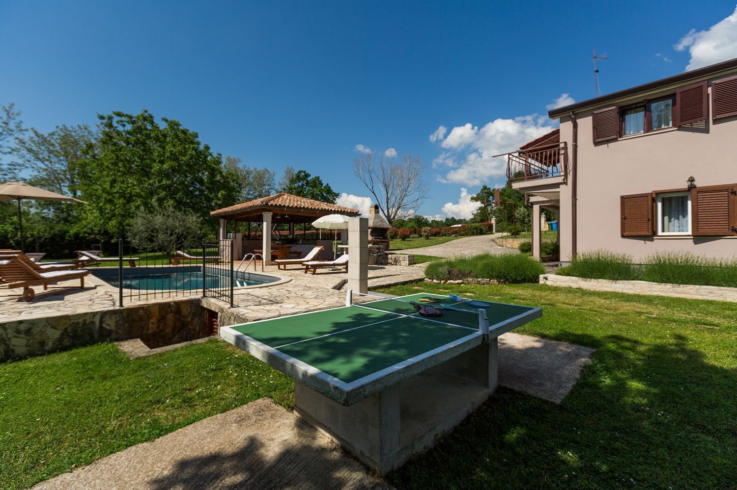 Ein Poolbereich mit Tischtennisplatte, Liegestühlen und einem Pavillon.