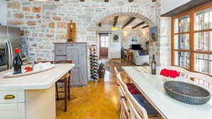 Une cuisine rustique aux murs de pierre, aux poutres apparentes et dotée d’un îlot central avec un meuble à vin.