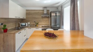 Une cuisine moderne avec des meubles blancs, un plan de travail en bois, un réfrigérateur en acier inoxydable et une table à manger sur laquelle se trouve un saladier rempli de fruits.