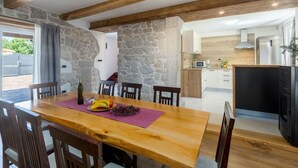 Un coin repas avec une table et des chaises en bois, un mur en pierre et une cuisine en arrière-plan.