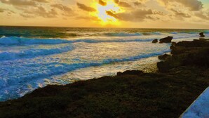 A coastal scene with waves crashing against rocks under a sunset sky.