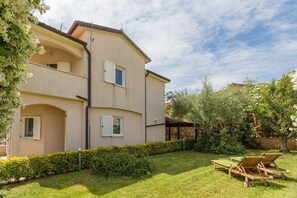 Stroll through the serene surroundings of this two-story residence, featuring a beautifully maintained lawn and a cozy patio area with lounge chairs and a table.