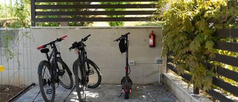 Et overdækket udendørsområde med to cykler og en elscooter parkeret op ad en væg.