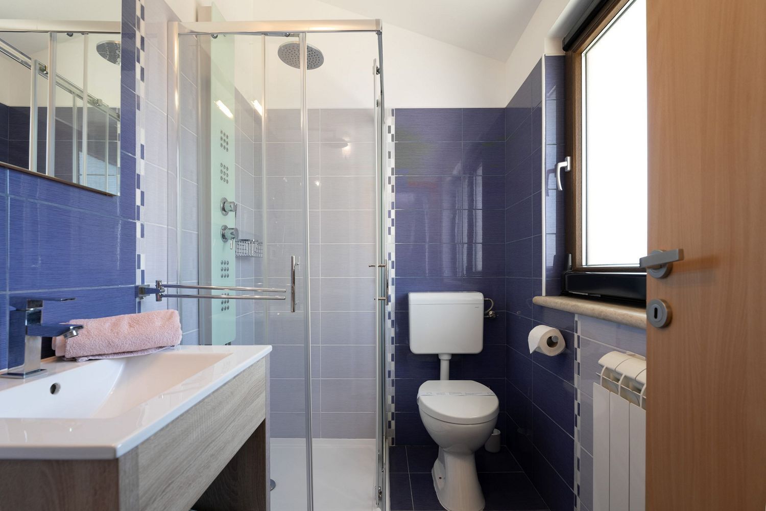 Un baño moderno con cabina de ducha de vidrio, inodoro blanco y lavamanos con una toalla rosa.