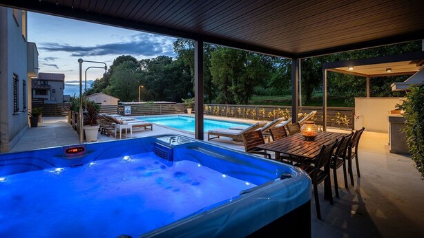 Un espace piscine extérieur abrité, doté de chaises longues et d’un jacuzzi.